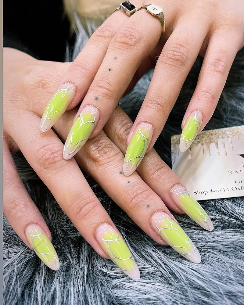 Lime aurora chrome stiletto nails with silver line art beside a Mii business card